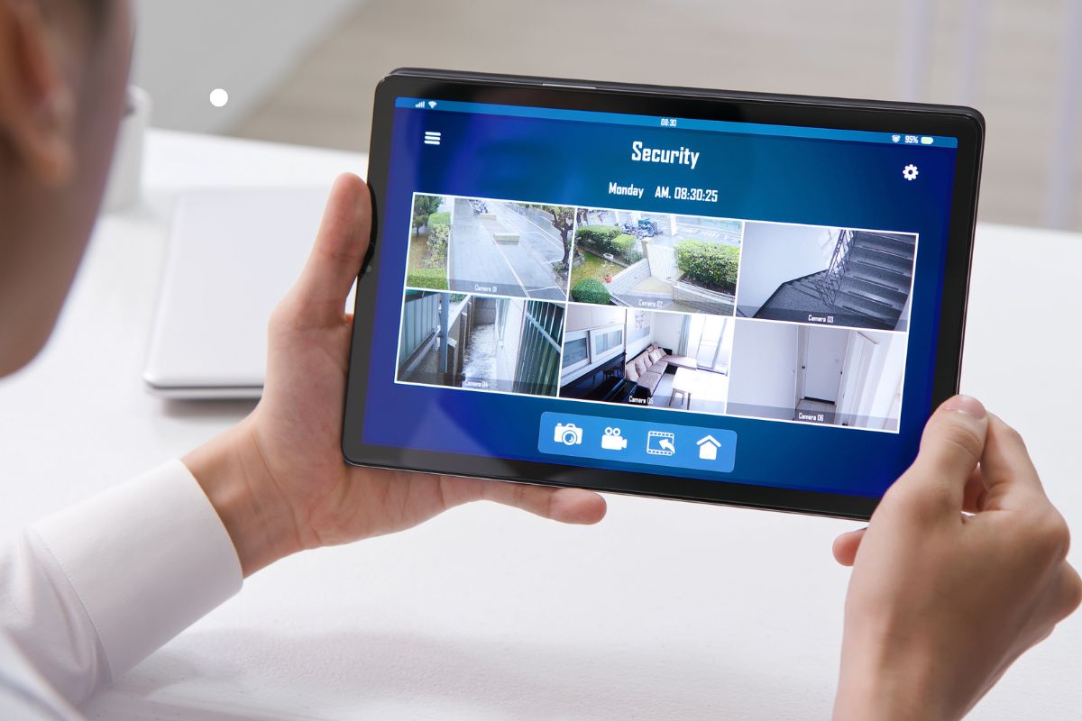 A person viewing a security camera feed on a tablet, displaying multiple camera angles of different locations.