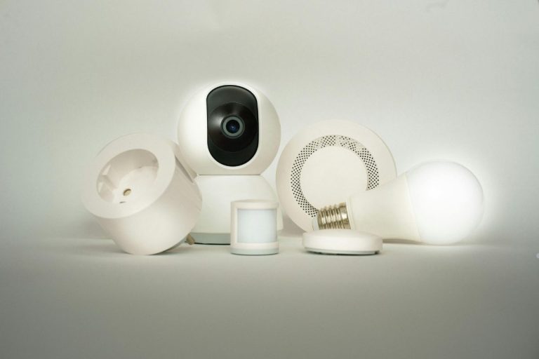 A collection of smart home devices, including a security camera, smart bulb, motion sensor, speaker, and smart plug, against a white backdrop.